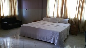 Una habitación de hotel con una cama grande, un sofá negro y una mesita de noche con una lámpara.