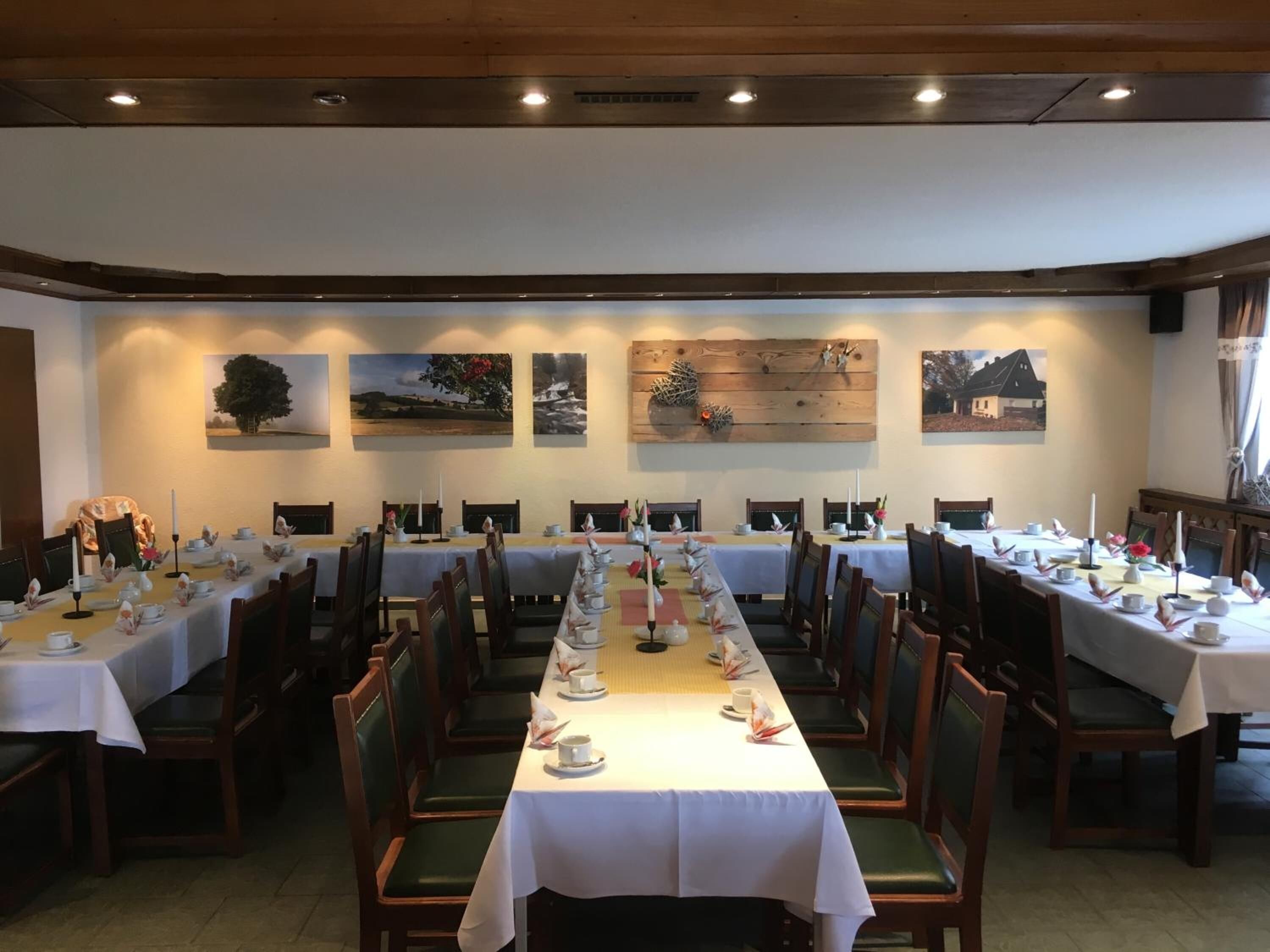 Ein Essbereich mit langen Tischen, die für eine Mahlzeit gedeckt sind, Holzsesseln und an der Wand befestigter Kunst.