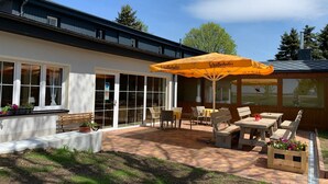 An outdoor patio area with tables and chairs, a large yellow umbrella, and a view of the building's exterior. - Hotel Dachsbaude & Kammbaude (Neuhausen)