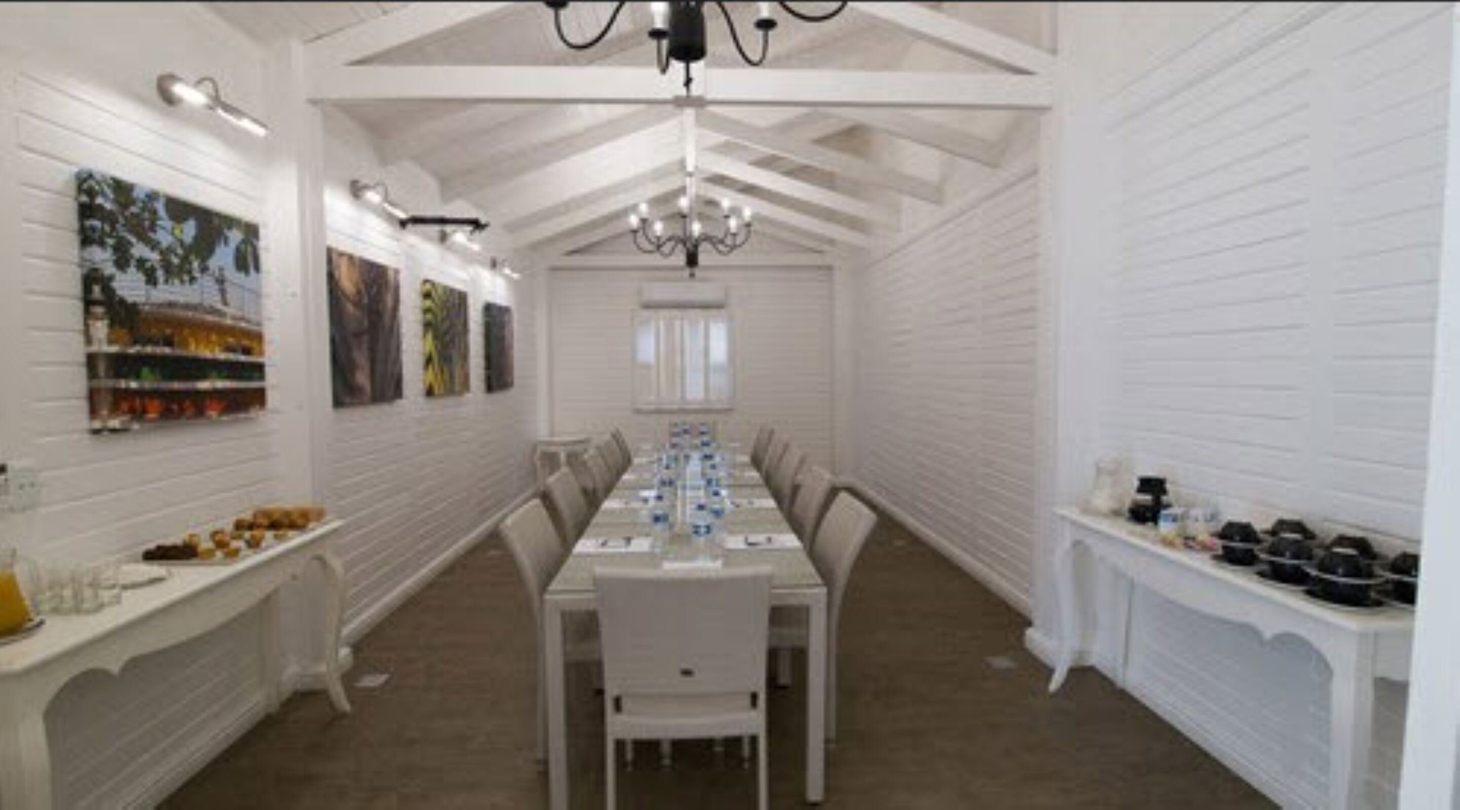 Comedor con una mesa larga, paredes blancas y una araña.