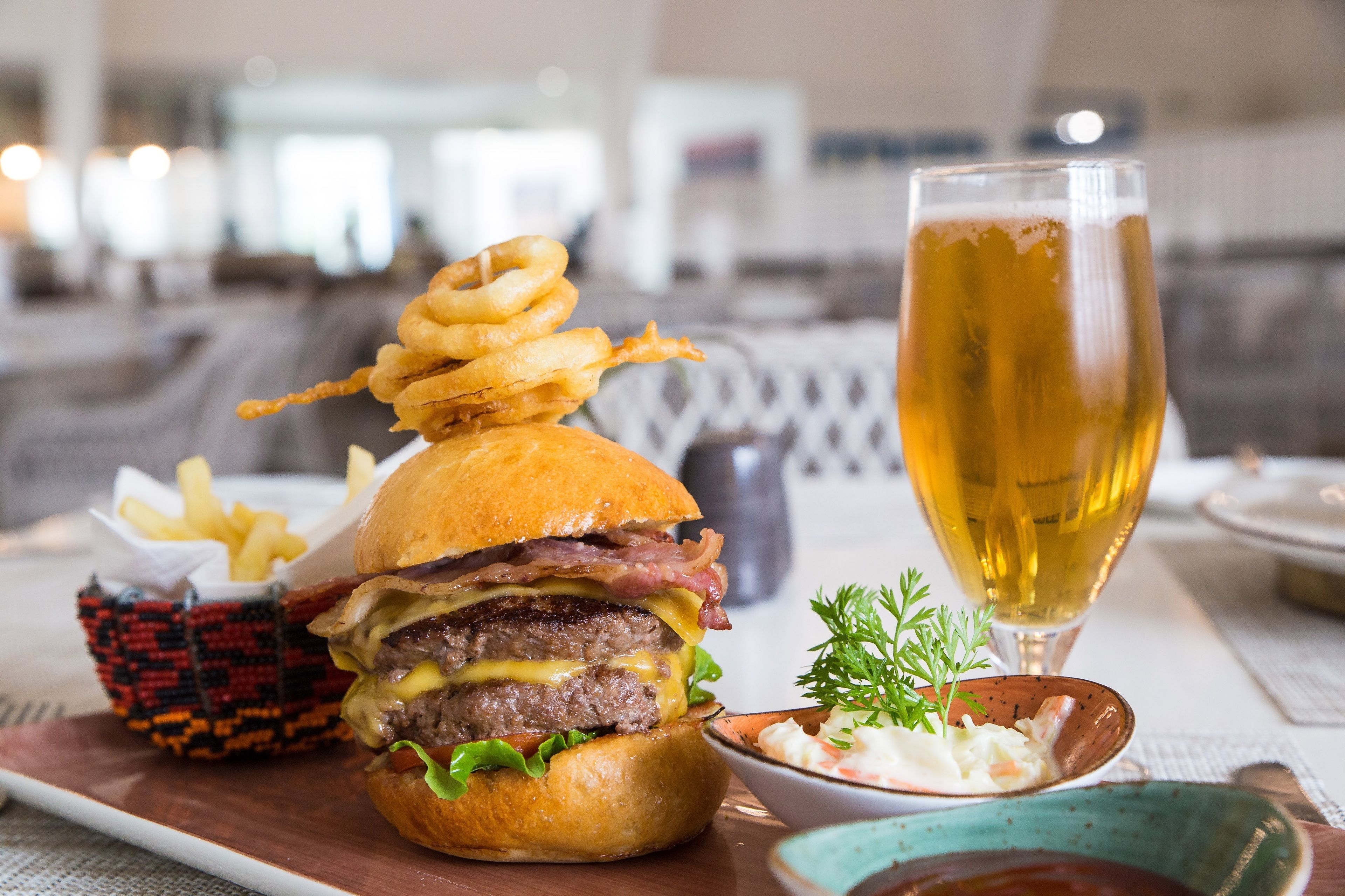 Un repas composé d’un hamburger, de rondelles d’oignon frites et d’un verre de bière, le tout sur une table.