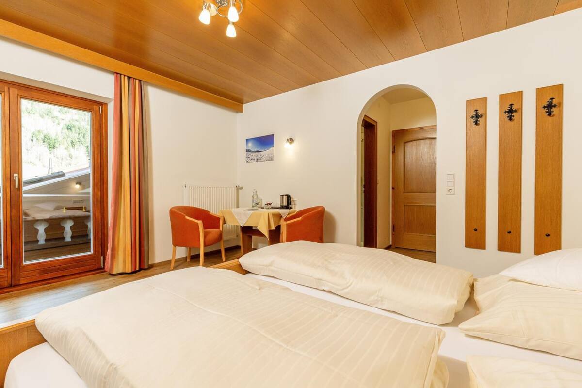 Une chambre d’hôtel avec deux lits, un bureau avec des chaises, une fenêtre avec des rideaux et une porte avec un panneau en bois.