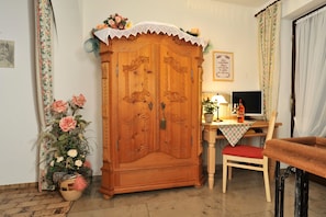 A wooden wardrobe with intricate carvings, a desk with a computer, and a chair. - Gästehaus Flora (Reit im Winkl)