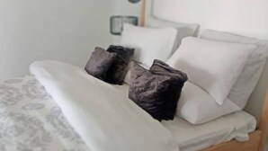 Een bed met witte lakens en donkere kussens.