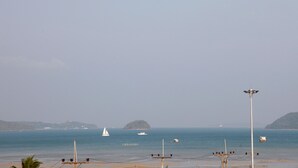 Una playa con un velero, una pequeña isla y un faro a lo lejos.
