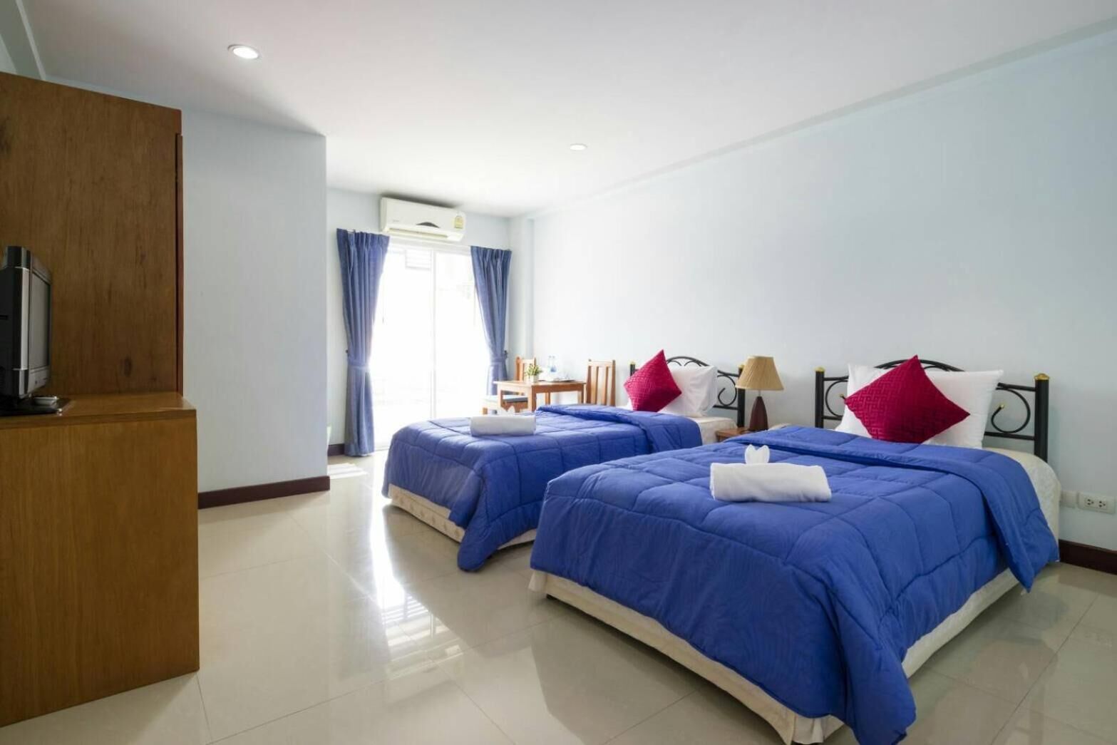 A hotel room with two beds, a wooden desk, a TV, and a window with curtains.