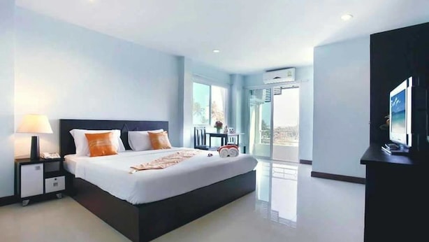 Una habitación de hotel moderna con una cama grande, mesitas de noche, un televisor y un balcón con vistas.