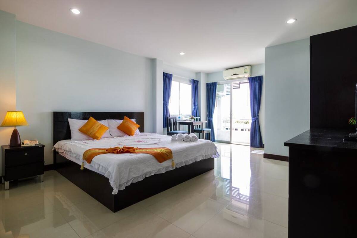 A hotel room with a large bed, a nightstand, a desk, and a view of the outside.