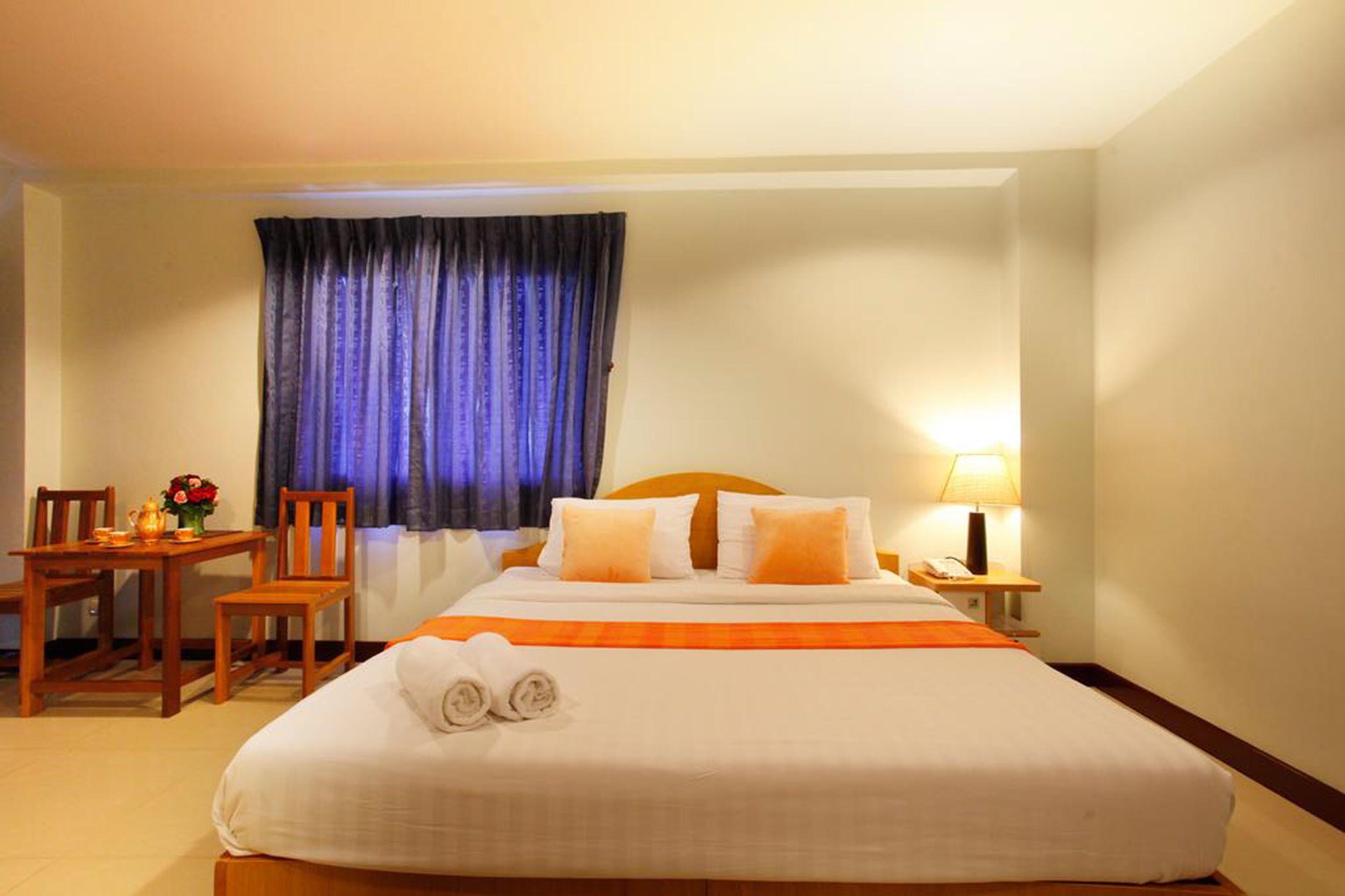 Habitación de hotel con una cama grande, un escritorio con silla, una lámpara y un ventanal con cortinas.
