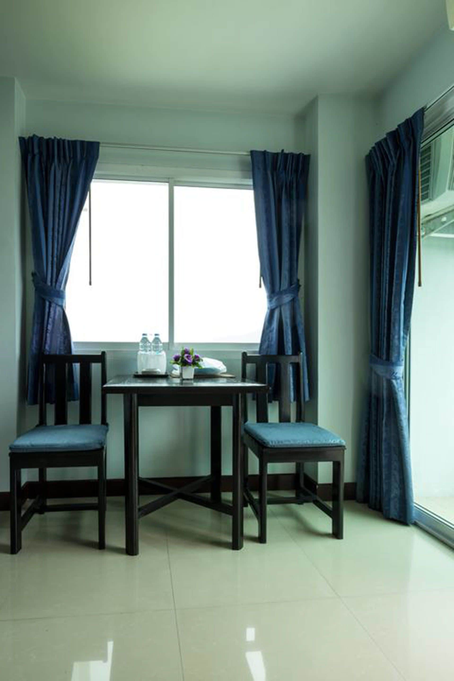 A room with a window, two chairs, a small table, and a water bottle.