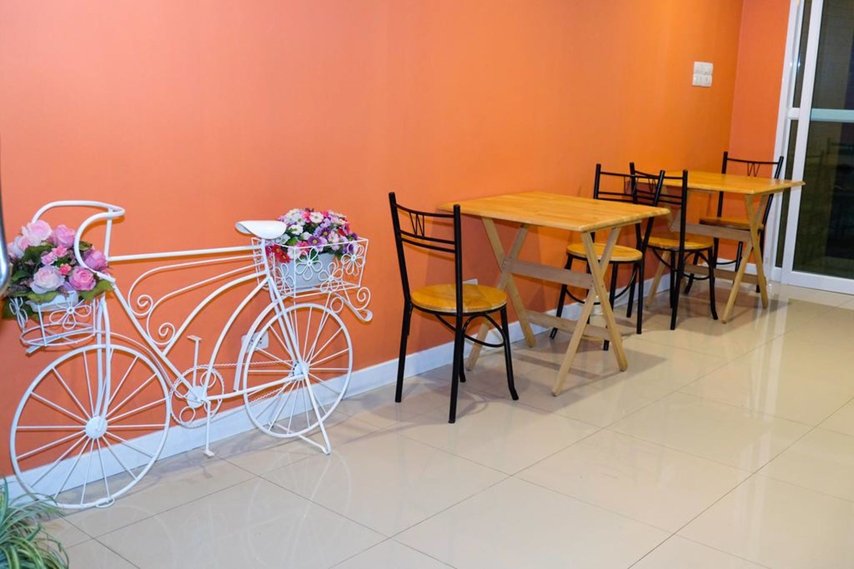 A dining area with a white bicycle, wooden tables, and chairs against an orange wall.