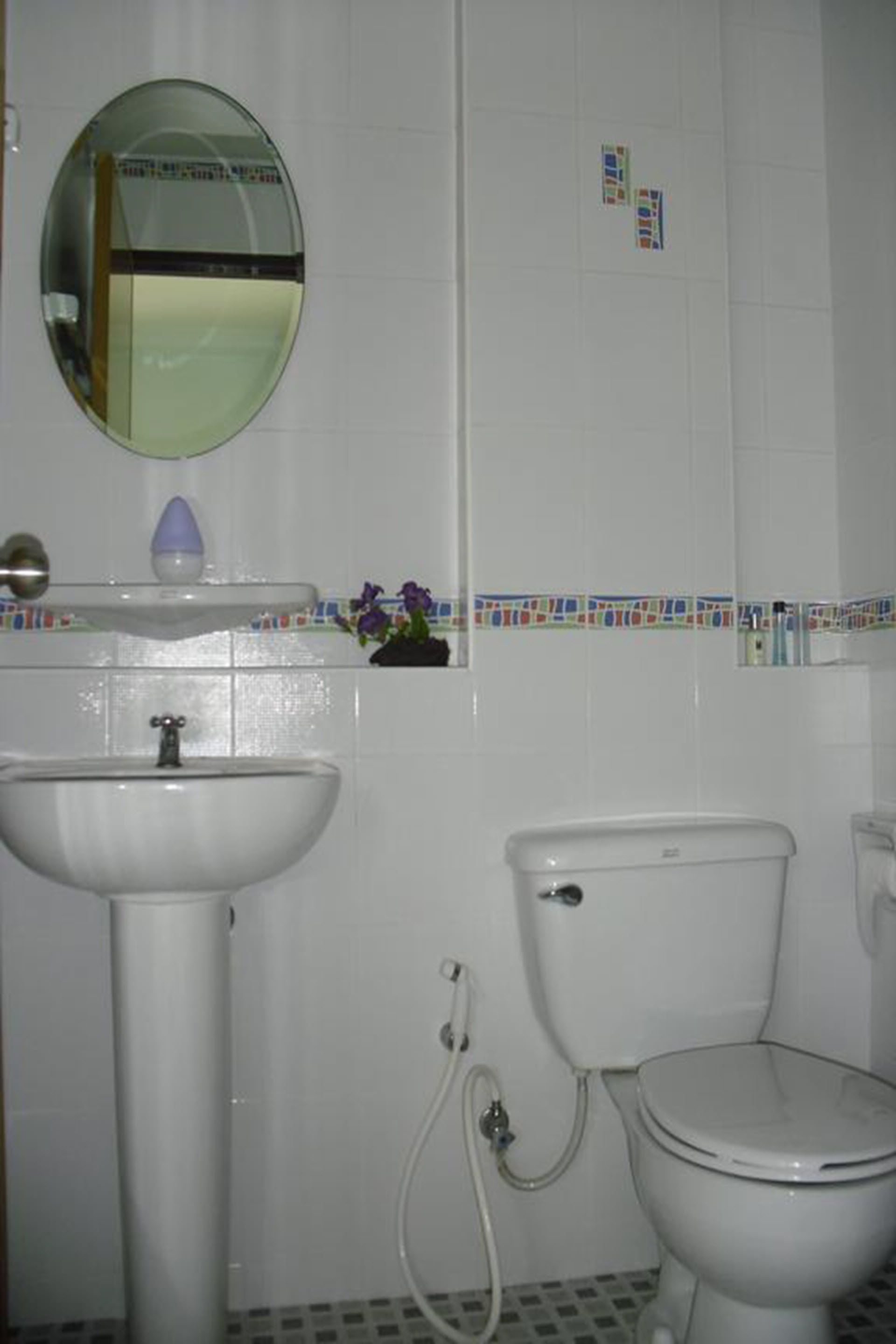 Une salle de bain avec un lavabo blanc, un miroir rond, des toilettes et une petite étagère contenant des articles de toilette.