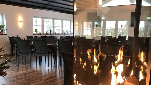 A restaurant with a glass partition separating the dining area from a fireplace. - Oldfruen De luxe (Vaeggerlose)