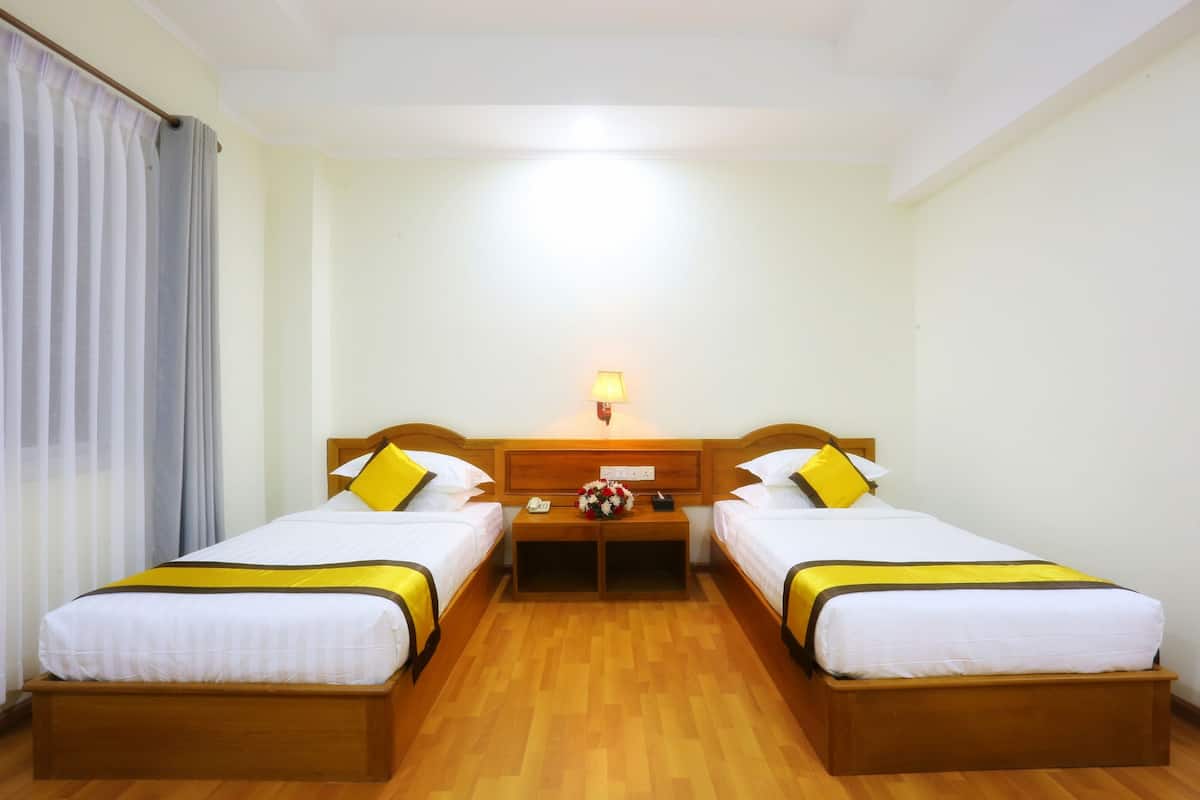 Ein Hotelzimmer mit zwei Einzelbetten, einem Nachttisch aus Holz mit Lampe und Holzboden.