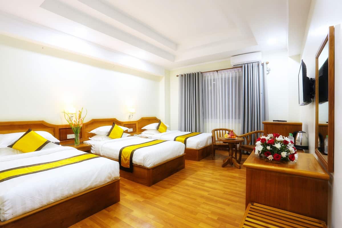 Ein Hotelzimmer mit zwei Einzelbetten, einem Holztisch, einem Stuhl, einem kleinen Tisch und einem an der Wand befestigten Fernseher.
