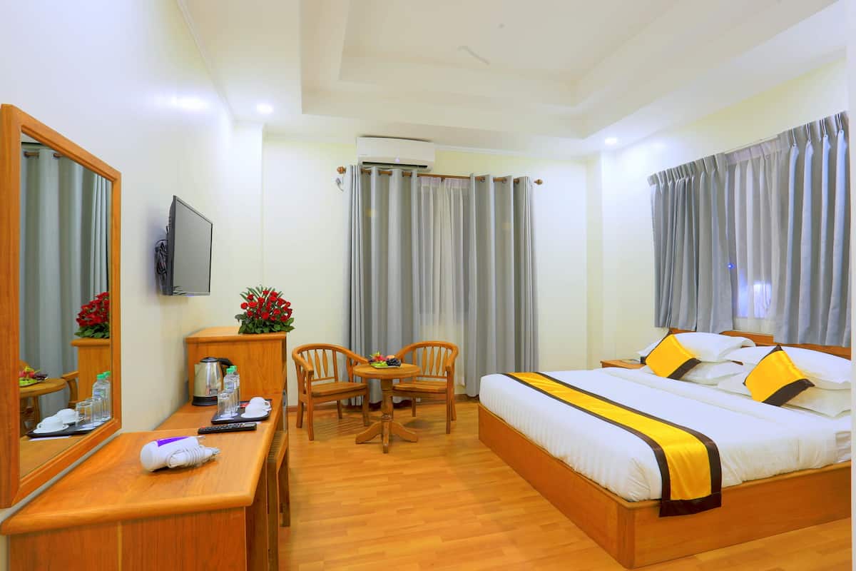Ein Hotelzimmer mit Bett, Schreibtisch mit Spiegel, Stuhl, kleinem Tisch mit Blume und Fernseher.