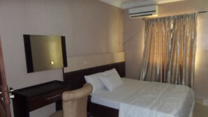 Una habitación de hotel con cama, escritorio, silla, equipo de aire acondicionado y cortina.