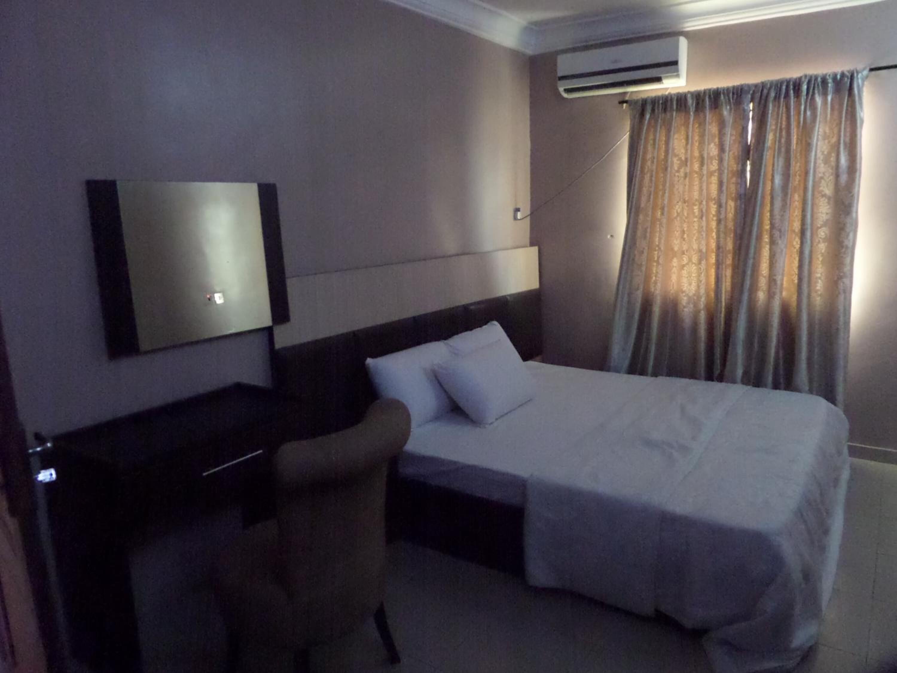Quarto de hotel com cama, escrivaninha, cadeira, ar condicionado e cortina.