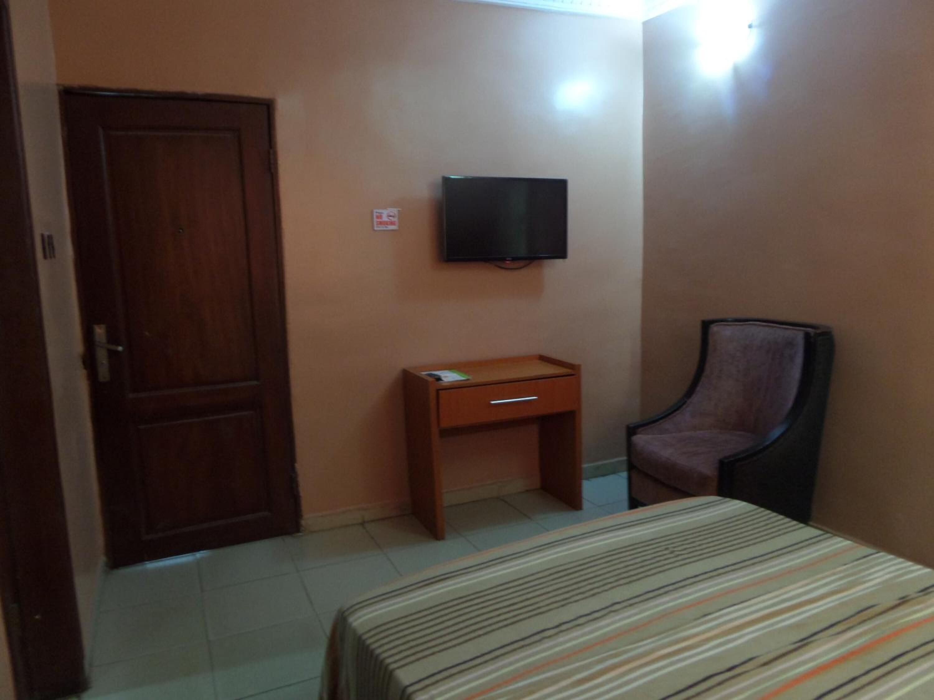 A small room with a bed, a desk, a chair, and a TV on the wall.