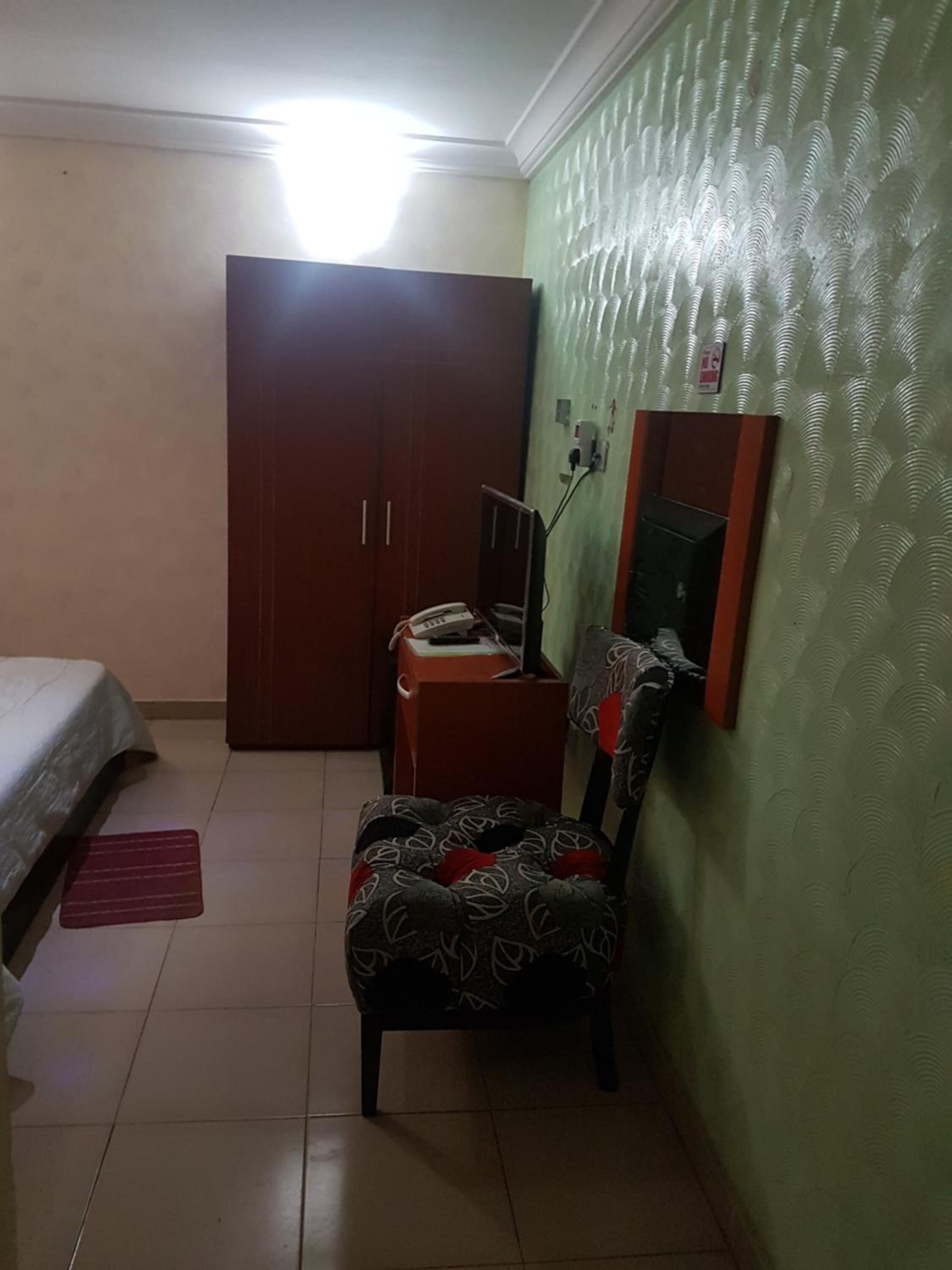 Una habitación pequeña y luminosa con cama, armario, silla y espejo en la pared.