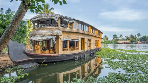 A houseboat with a covered deck, windows, and a railing, docked in a body of water surrounded by greenery. - GuestHouser 3 BHK Houseboat e567 (Kuttanad Taluk)