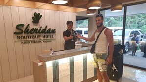 Een receptiebalie bij het Sheridan Boutique Hotel, met een bord dat de locatie in Puerto Princesa, Palawan aangeeft.