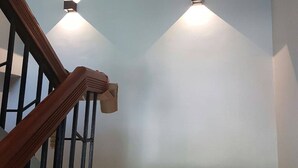 Een trap met houten leuningen en zwarte metalen balustrades, die uitkomt op een plateau met twee wandlampen.