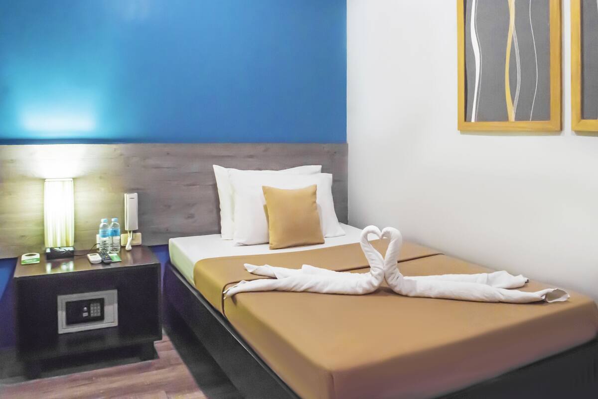 Een hotelkamer met een bed, een nachtkastje met een lamp en een kunstwerk aan de muur.