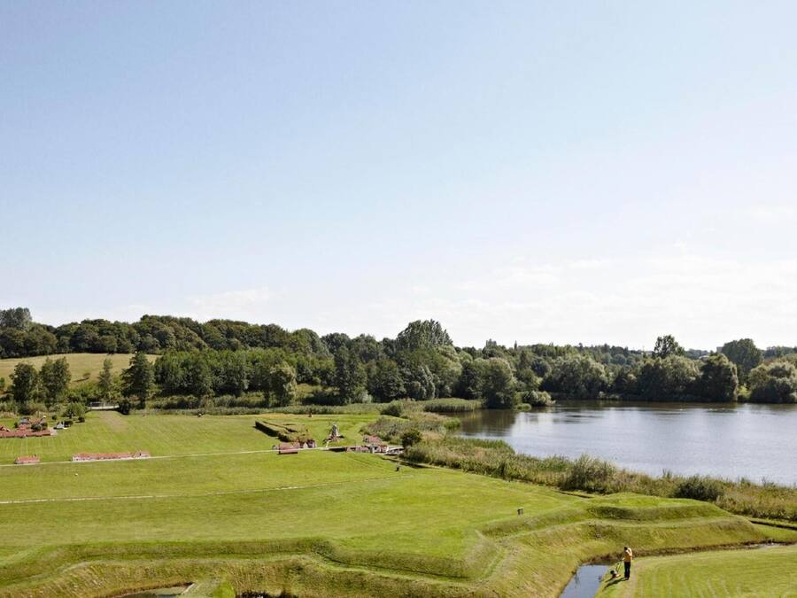 Un campo de golf con un lago, praderas verdes y edificios dispersos.