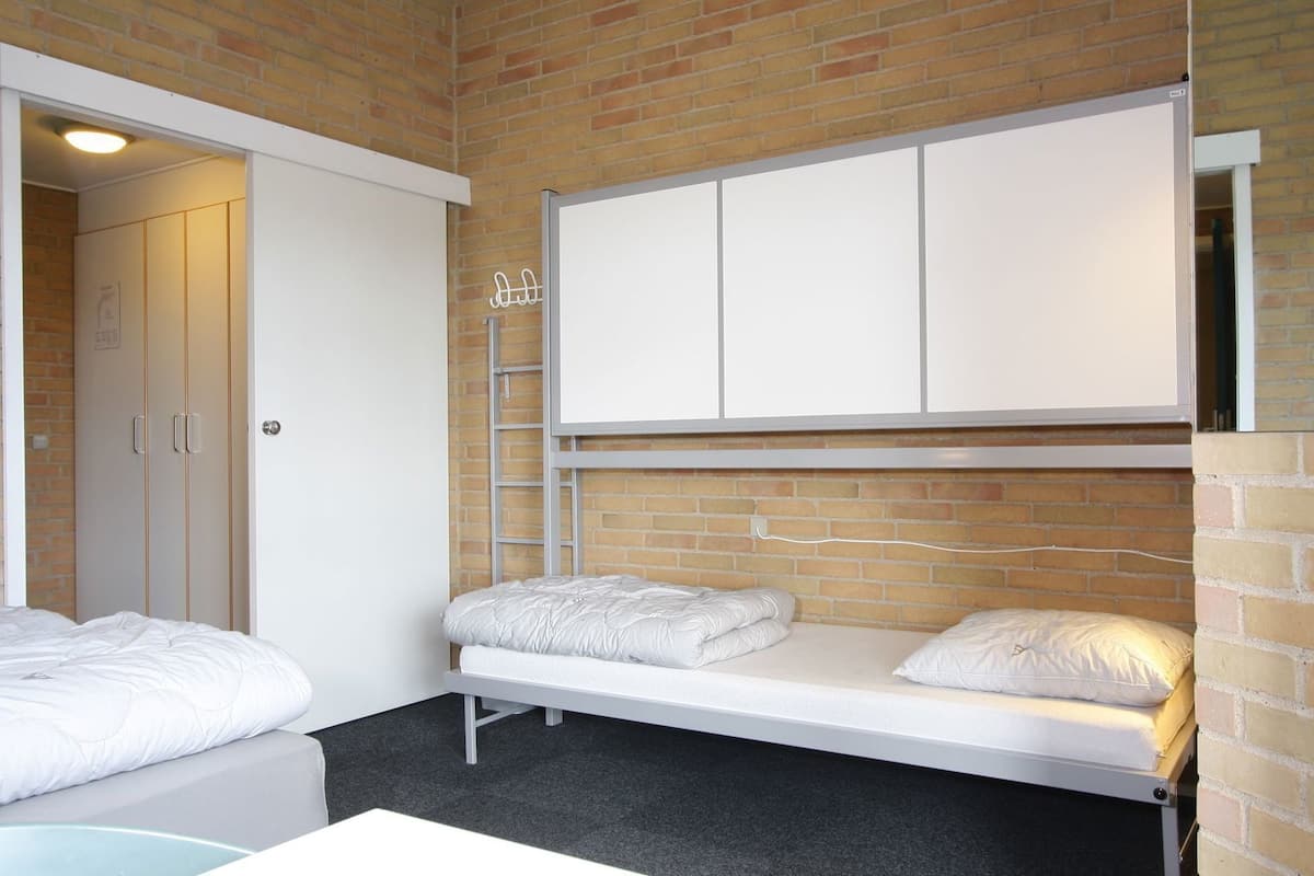 Una habitación con cama, una mesita, un armario y una pizarra blanca en la pared.