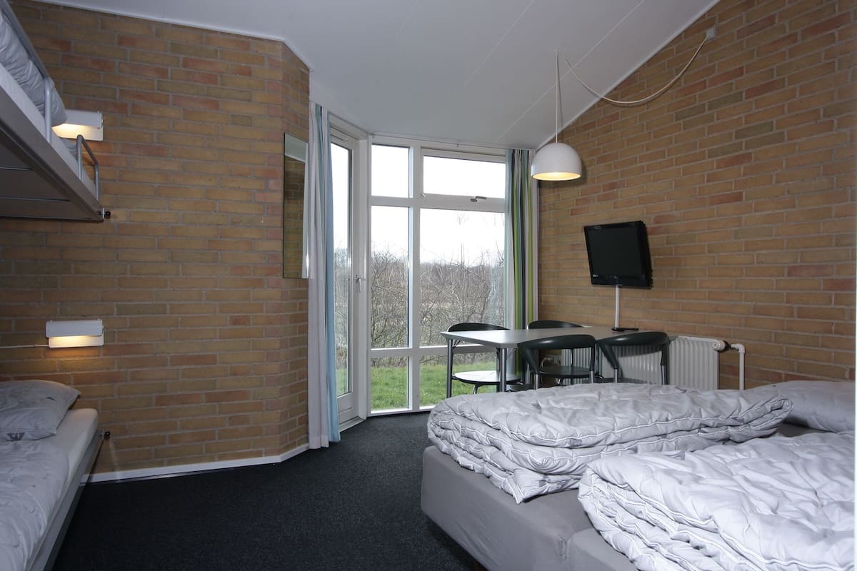Un dormitorio con pared de ladrillo, un escritorio, una silla, una cama y un televisor.