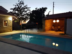 A swimming pool with a ladder, surrounded by stone walls and a tree. There are outdoor chairs and a table under a lamp. - A Casa do Professor (Carrazeda de Ansiaes)