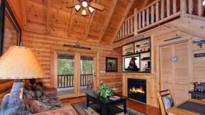 Ein gemütliches Blockhaus-Interieur mit Kamin, einer Couch, einem Couchtisch und einem Essbereich.