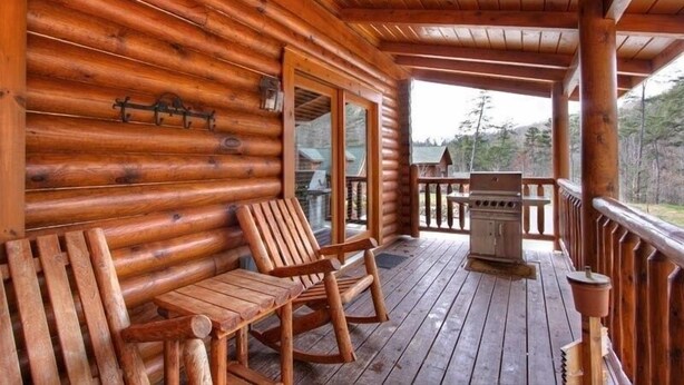 Eine Holzhütte mit Veranda, zwei Schaukelstühlen und einem Grill.