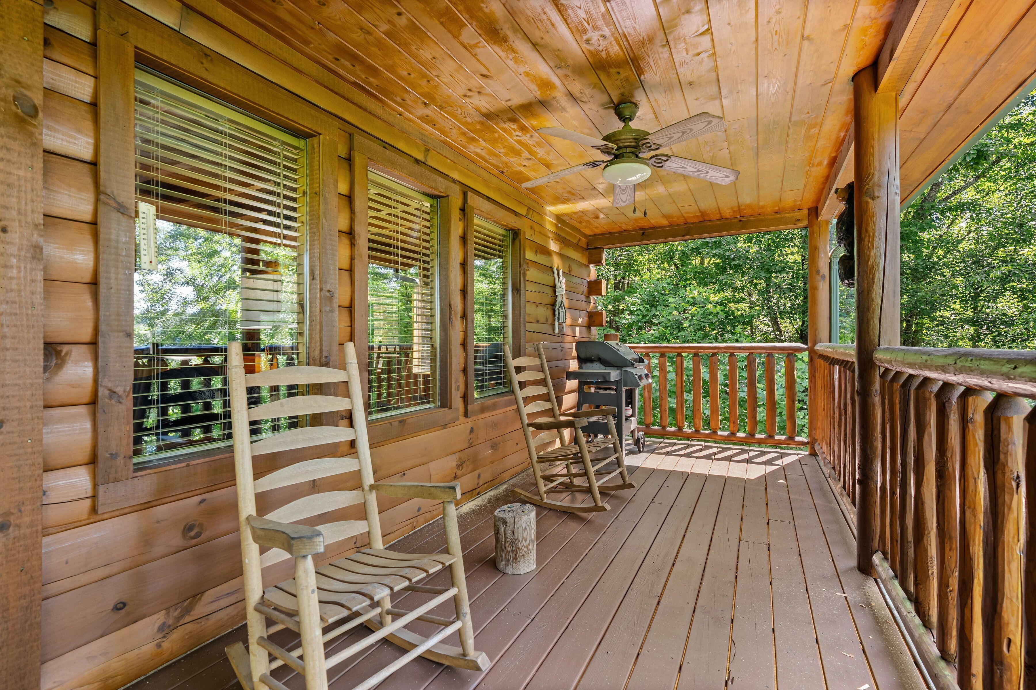 A wooden porch with rocking chairs, a grill, and a ceiling fan.