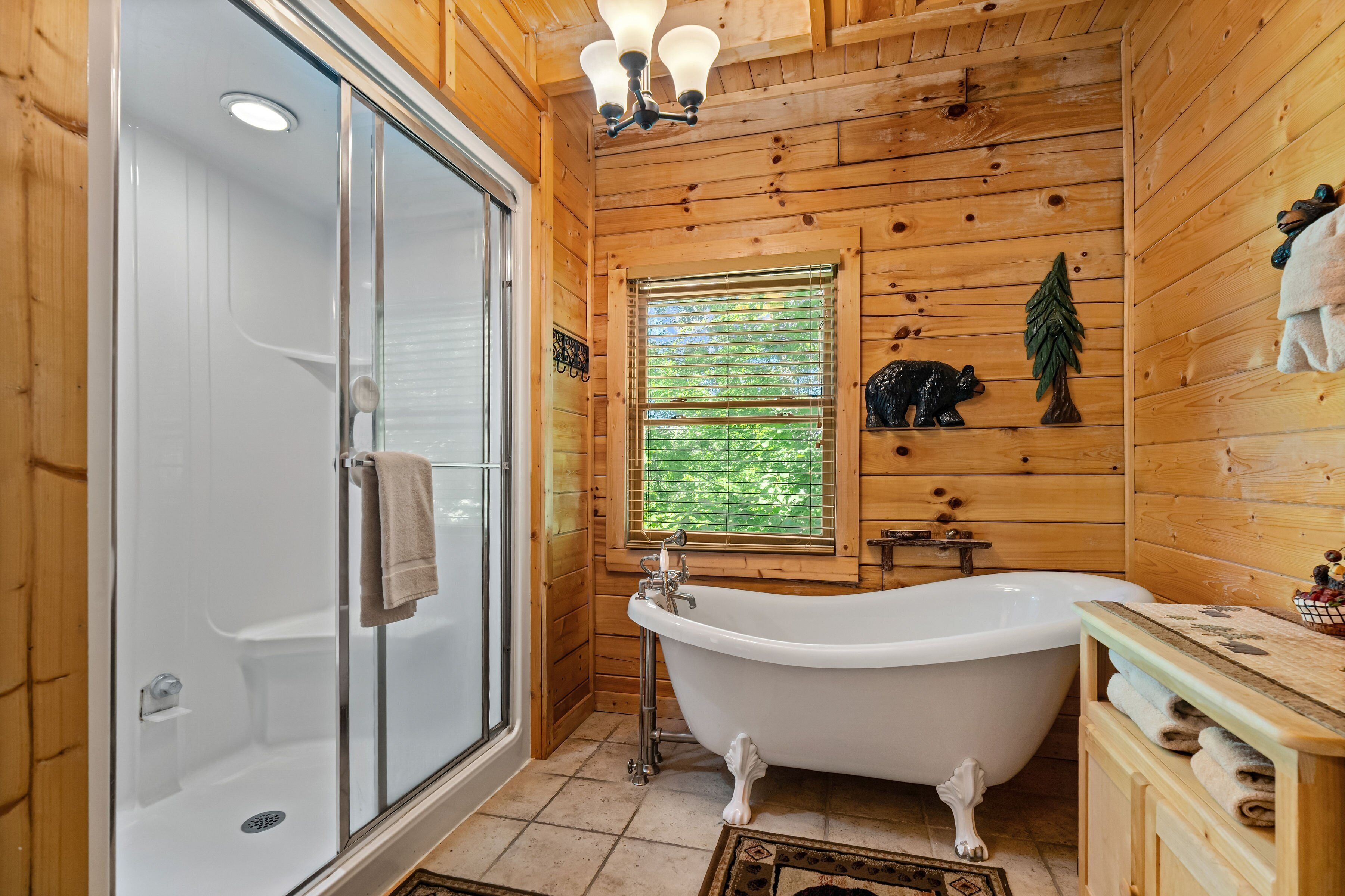 A wooden cabin bathroom with a glass-enclosed shower, a freestanding bathtub, and a window with blinds.