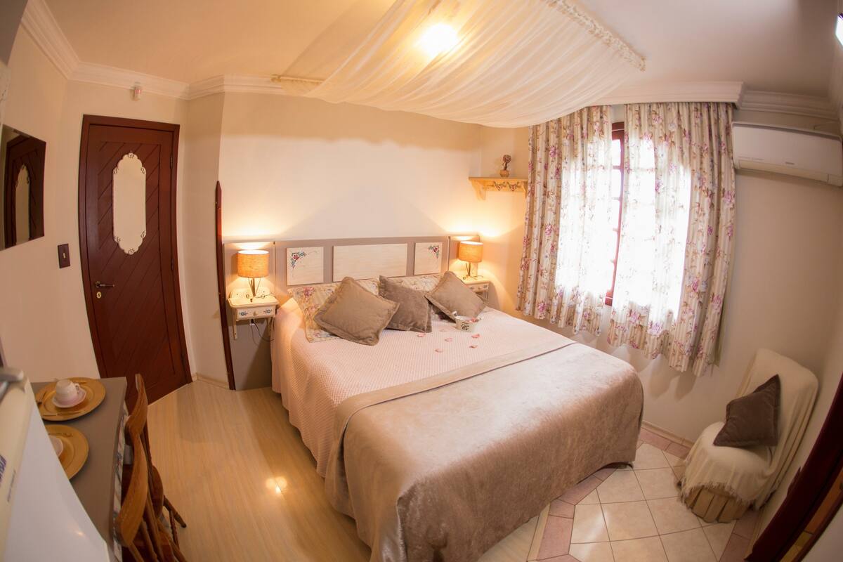 Une chambre à coucher avec un grand lit, des lampes de chevet, une chaise, une petite table avec une tasse et une soucoupe, et une porte.