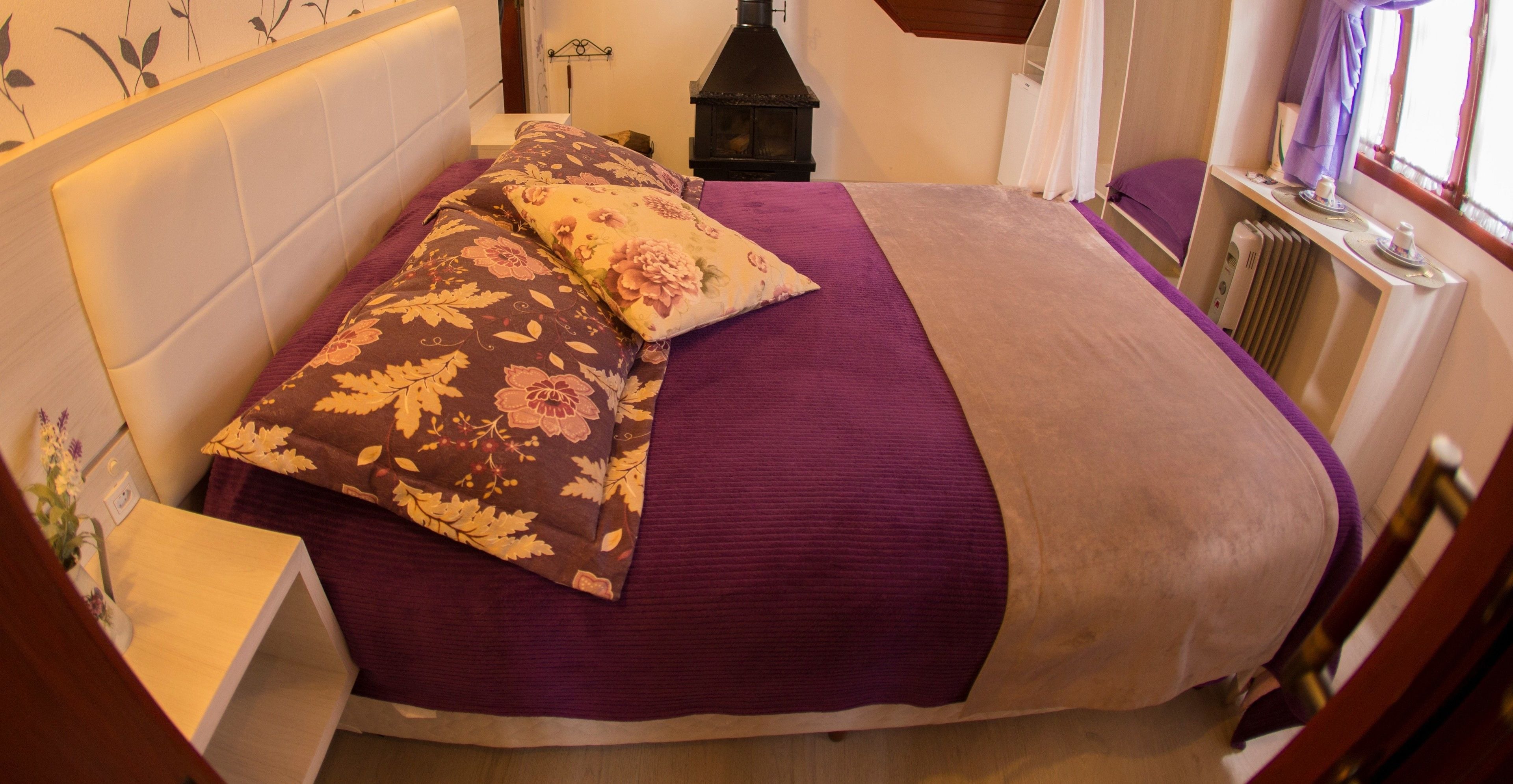 A bed with floral pillows, a purple bedspread, and a wooden headboard.