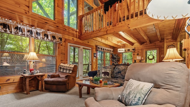 A cozy log cabin interior with a large window, a wooden staircase, and a comfortable seating area. - Forest Fling 2 Bedroom Cabin by RedAwning (Sevierville)