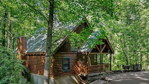 A log cabin with a porch and a small deck, surrounded by dense forest. - Forest Fling 2 Bedroom Cabin by RedAwning (Sevierville)
