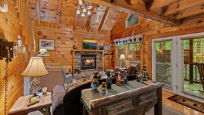 A cozy cabin interior with a fireplace, wooden walls, a desk with bear figurines, and a large window with blinds. - Forest Fling 2 Bedroom Cabin by RedAwning (Sevierville)
