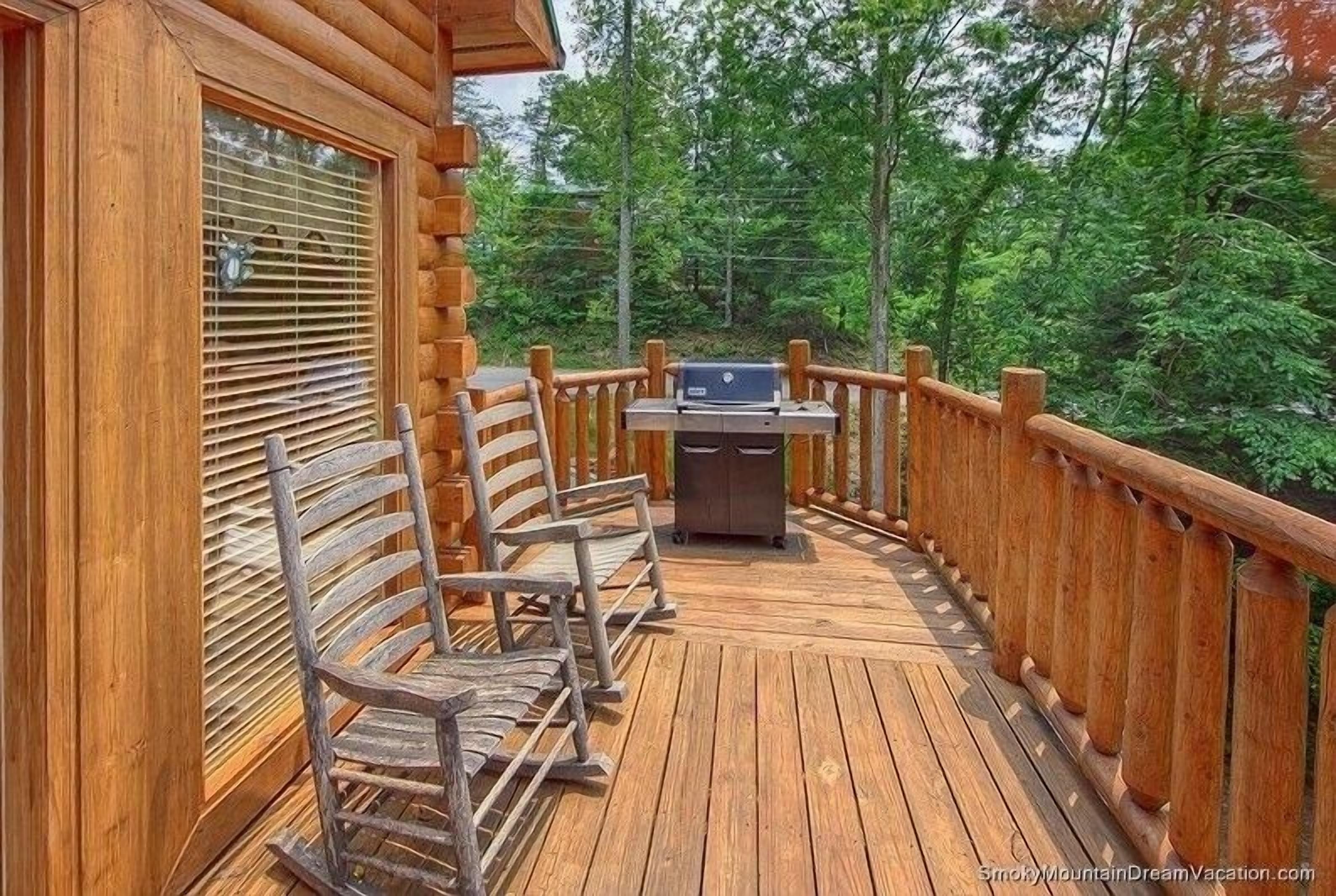 A wooden deck with a grill and two metal chairs.
