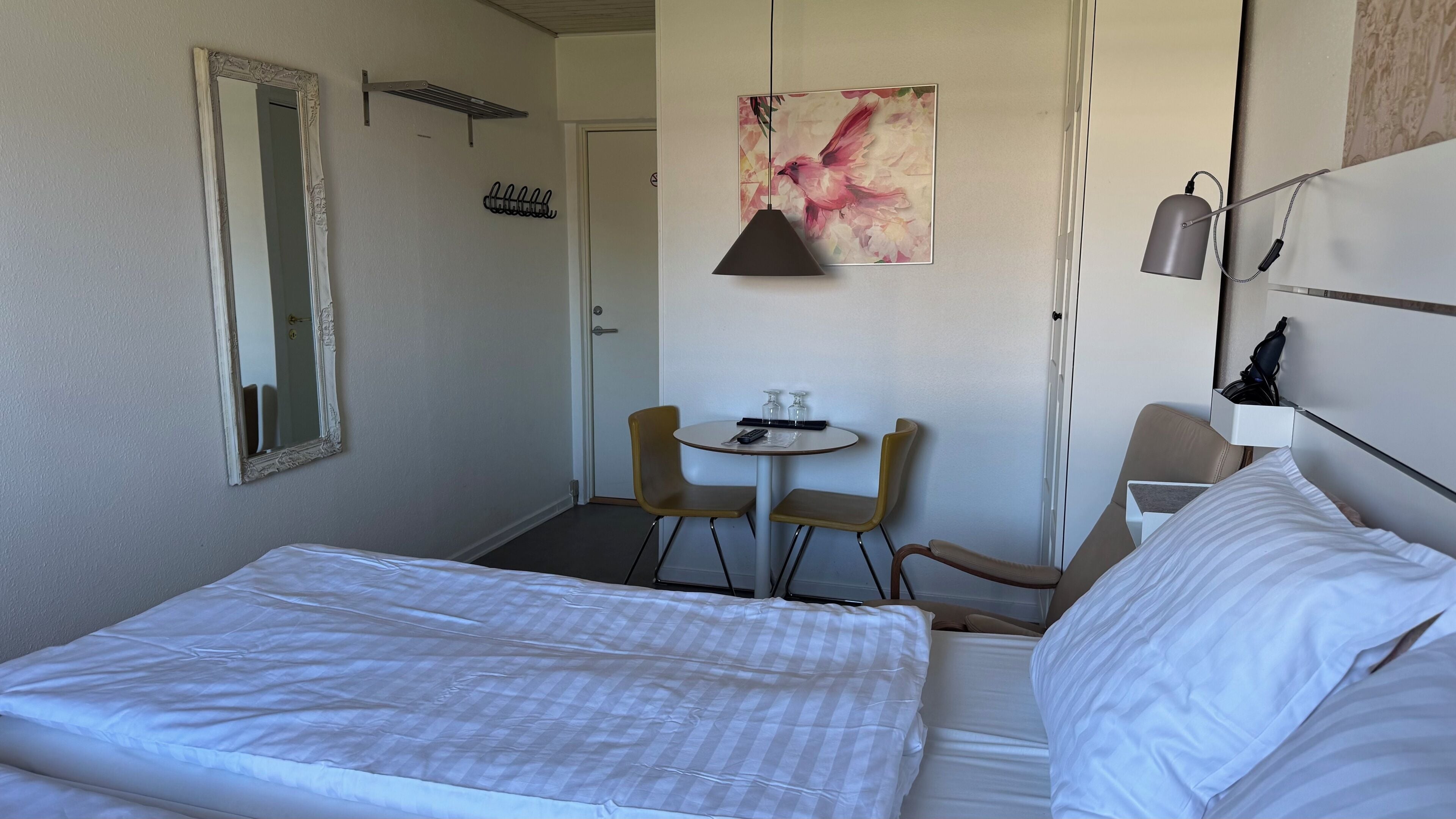 Ein Hotelzimmer mit einem Bett, einem kleinen runden Tisch mit Stühlen, einem Spiegel, einer Wandleuchte und einem Bild.