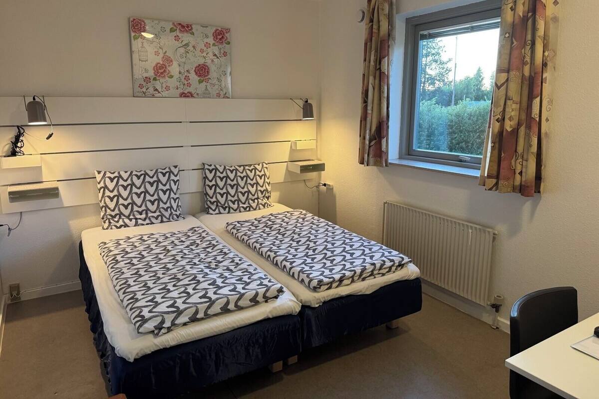Ein Schlafzimmer mit zwei Betten, einem fenster mit Vorhängen, einem Heizkörper und einem Wandbild.