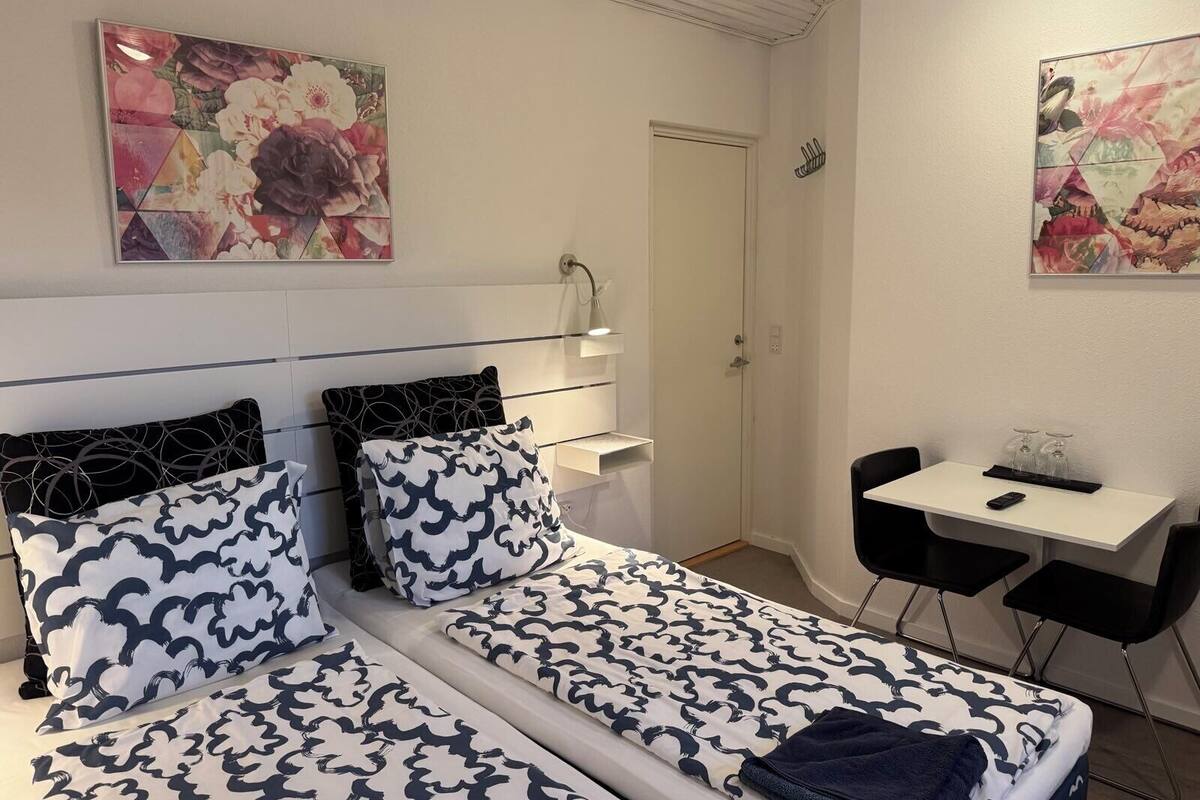 Ein Hotelzimmer mit zwei Betten, einem Schreibtisch und einem Sessel. An den Wänden hängen zwei Gemälde.