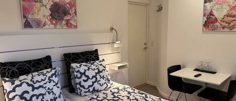 A hotel room with two beds, a desk, and a chair. There are two paintings on the walls.