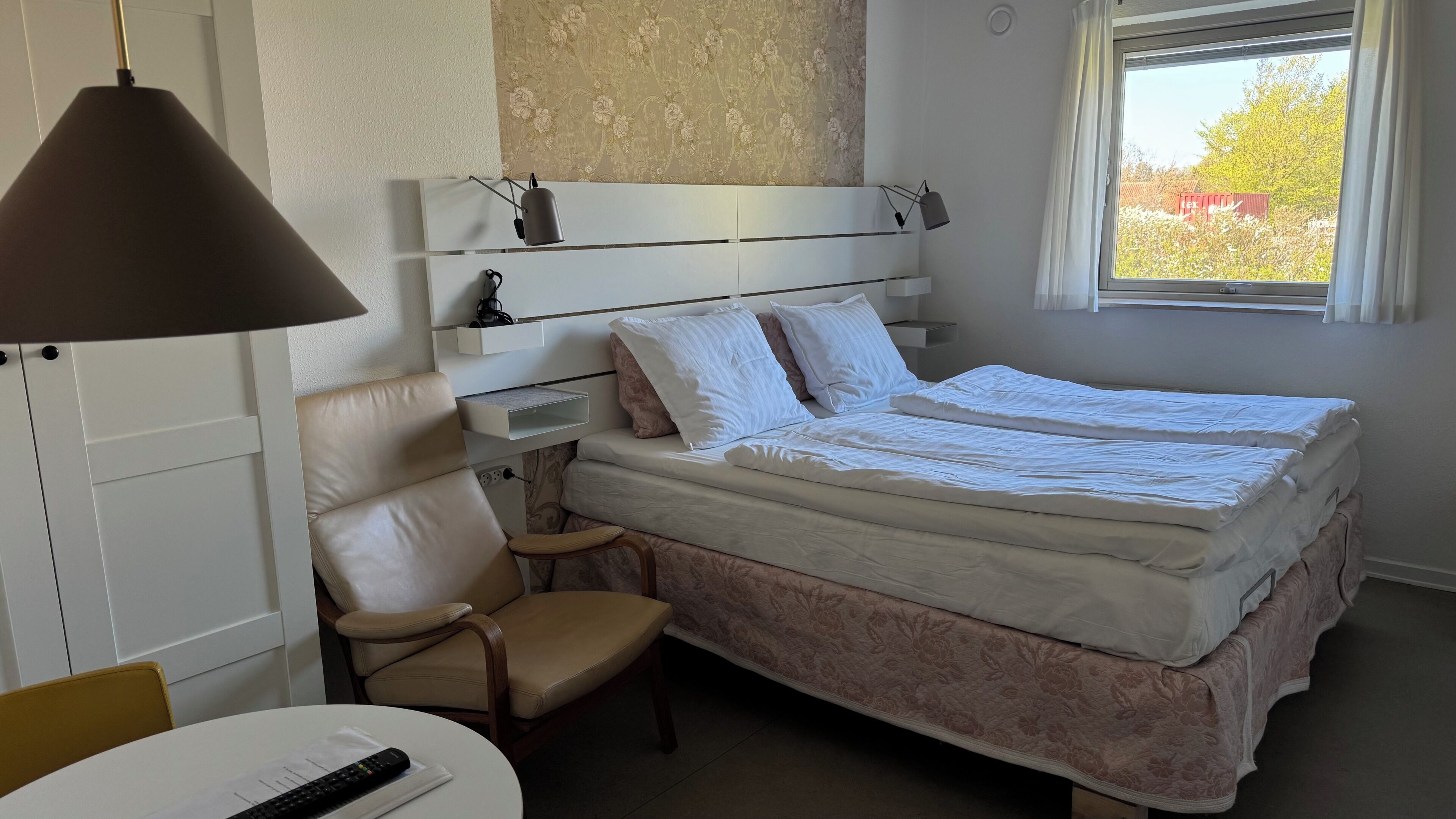 Un dormitorio con cama, una silla, un escritorio, una lámpara y una ventana.