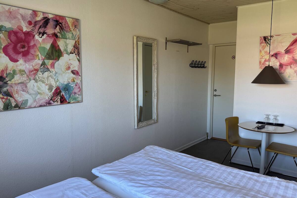 Ein Hotelzimmer mit einem Bett, einem kleinen Tisch mit Stühlen, einem Spiegel und einem Blumenbild an der Wand.