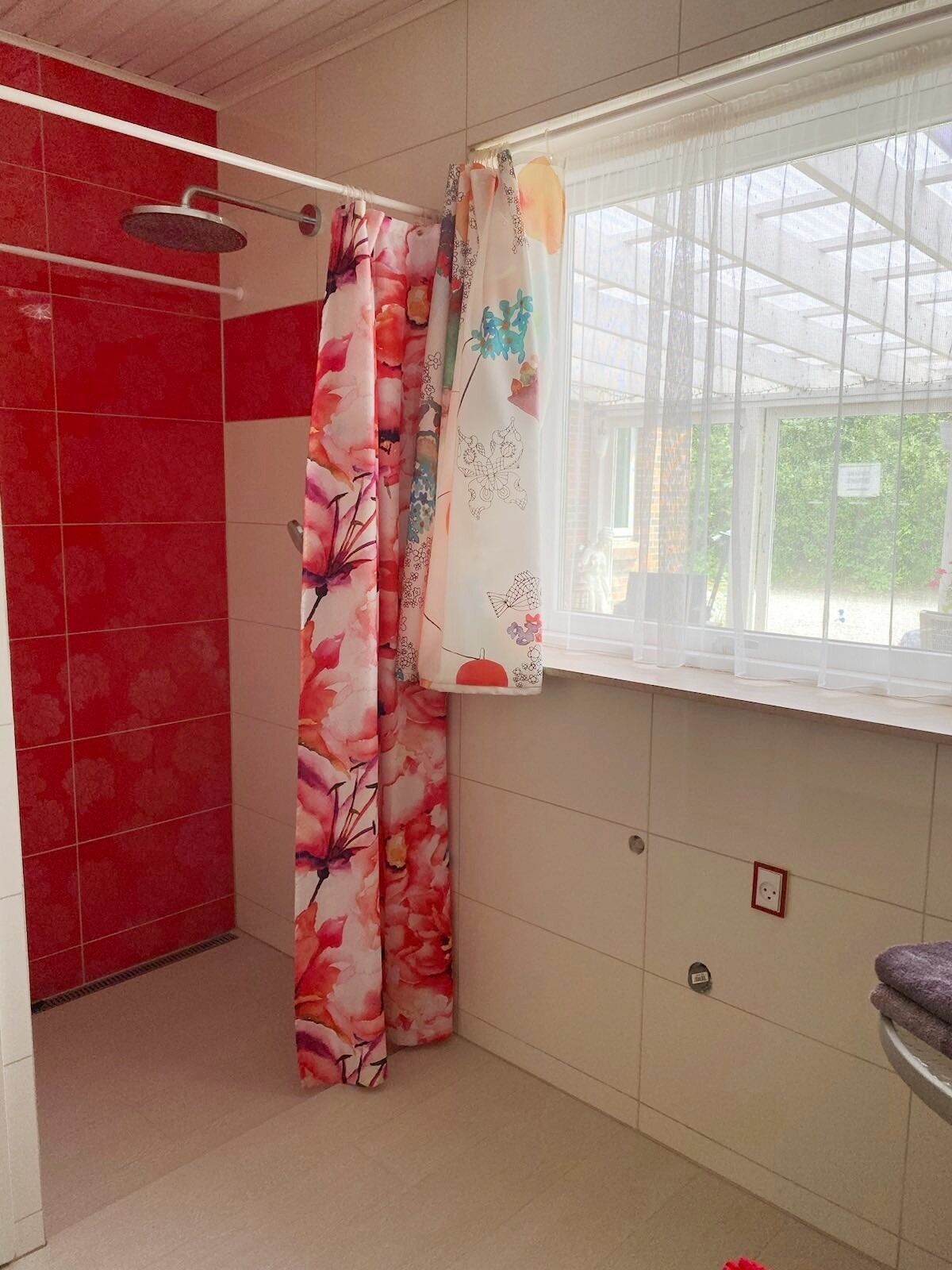Ein Badezimmer mit Dusche, einem Fenster mit Ausblick und einem gefliesten Boden.