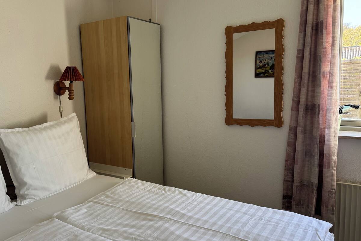 Ein Hotelzimmer mit Bett, Kleiderschrank, Spiegel und einem Fenster mit Vorhängen.